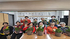 책상 앞에 모여 앉아서 각각 화분을 들고 포즈를 취하고 있는 노인들 모습