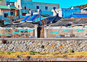 벽면에 그림이 그려져 있고 그 뒷편에 파란 지붕에 집과 건물들이 있는 사진