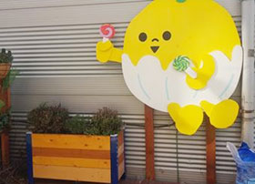 나무재질로 되어진 화분에 잔디가 심어져 있고 벽면에는 사탕을 들고 있는 노란 배 캐릭터가 붙어있다.