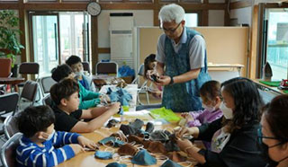 남자 어르신이 어린아이들이게 쳔연으로 만든 마스크를 제공하여 교육하고 있는 모습