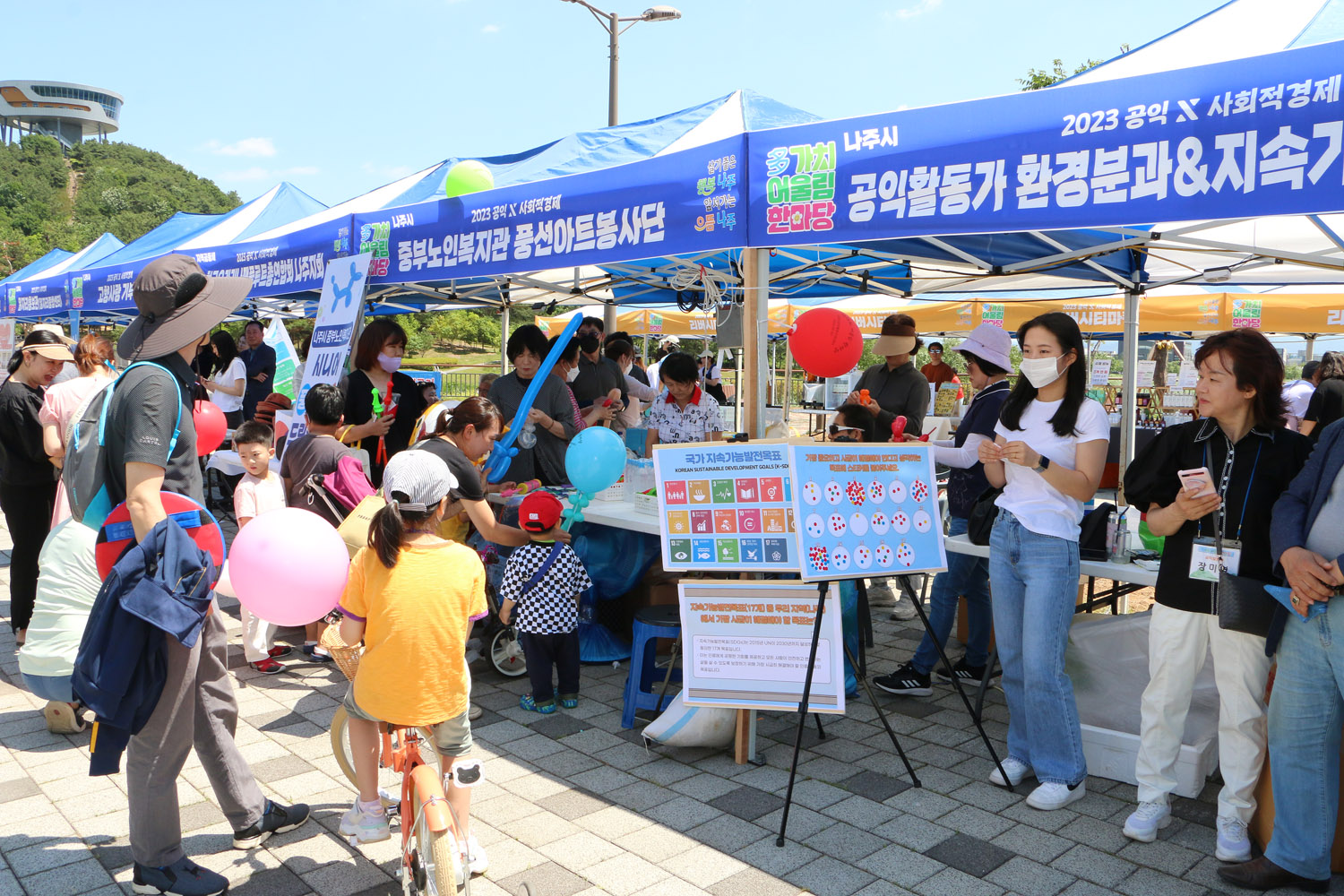 多가치 어울림 한마당 기념식 행사장 부스에 마련된 풍선아트 봉사단 앞에 어린이를 동반한 가족들이 부적이는 모습