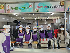 봉사를 실천하는 행복한 식당을 만들겠습니다. 라고 써진 경로식당 내부에서 위생모와 앞치마를 착용하고 배식을 하고 있는 사람들 모습