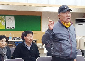 어르신이 일어나 집게손가락을 들며 말씀하시는 모습
