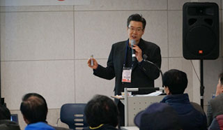 정장을 차려입은 남자가 마이크를 들고 설명하는 모습