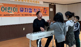 피아노치는 남자선생님과 어린이 세명이 노래 부르고 있는 모습