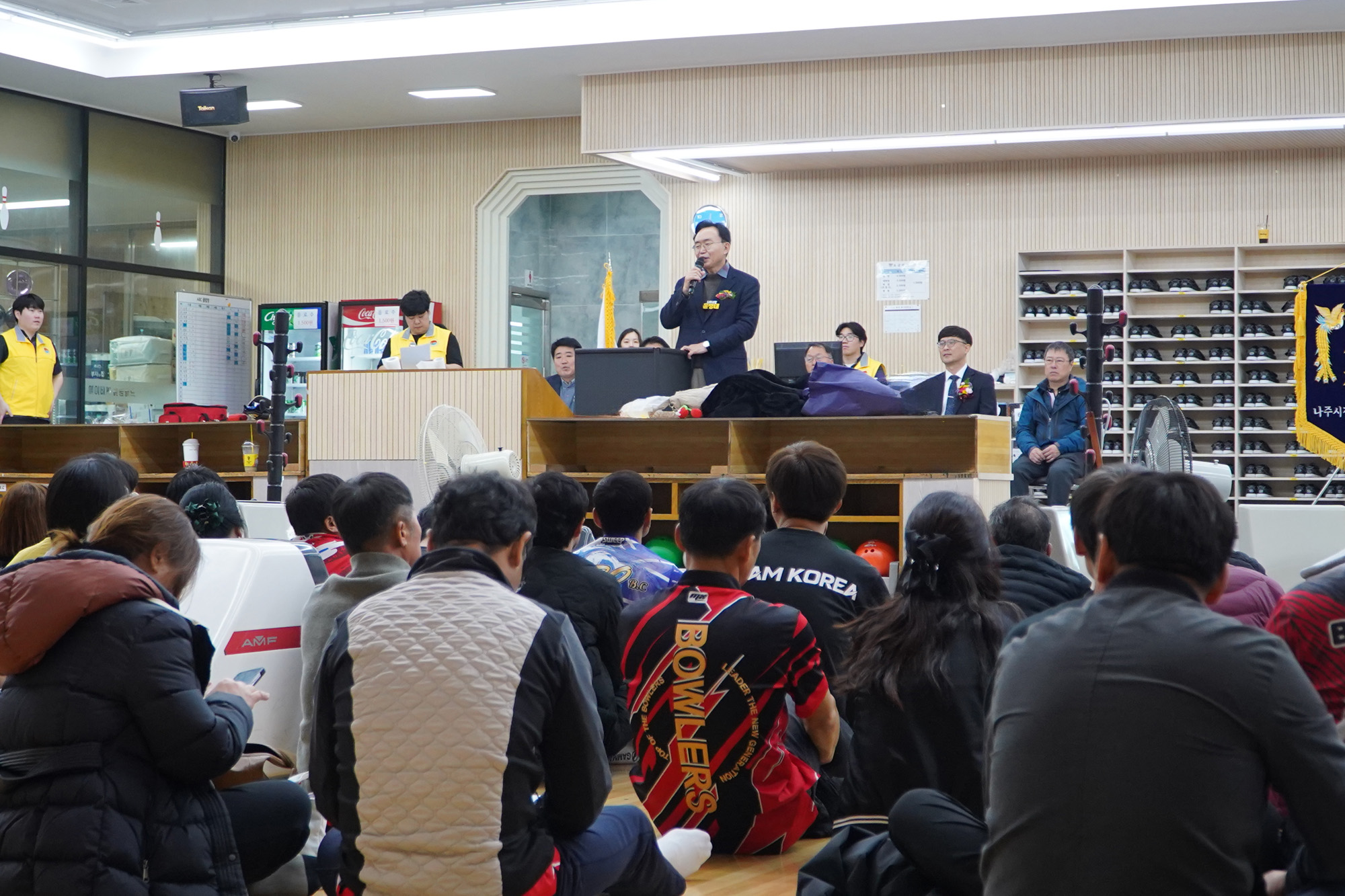  윤병태 나주시장이 무대 위에 올라 연설하고 있고, 많은 관람객들이 바닥에 앉아 연설자를 바라보고 있는 볼링장 내부 전경