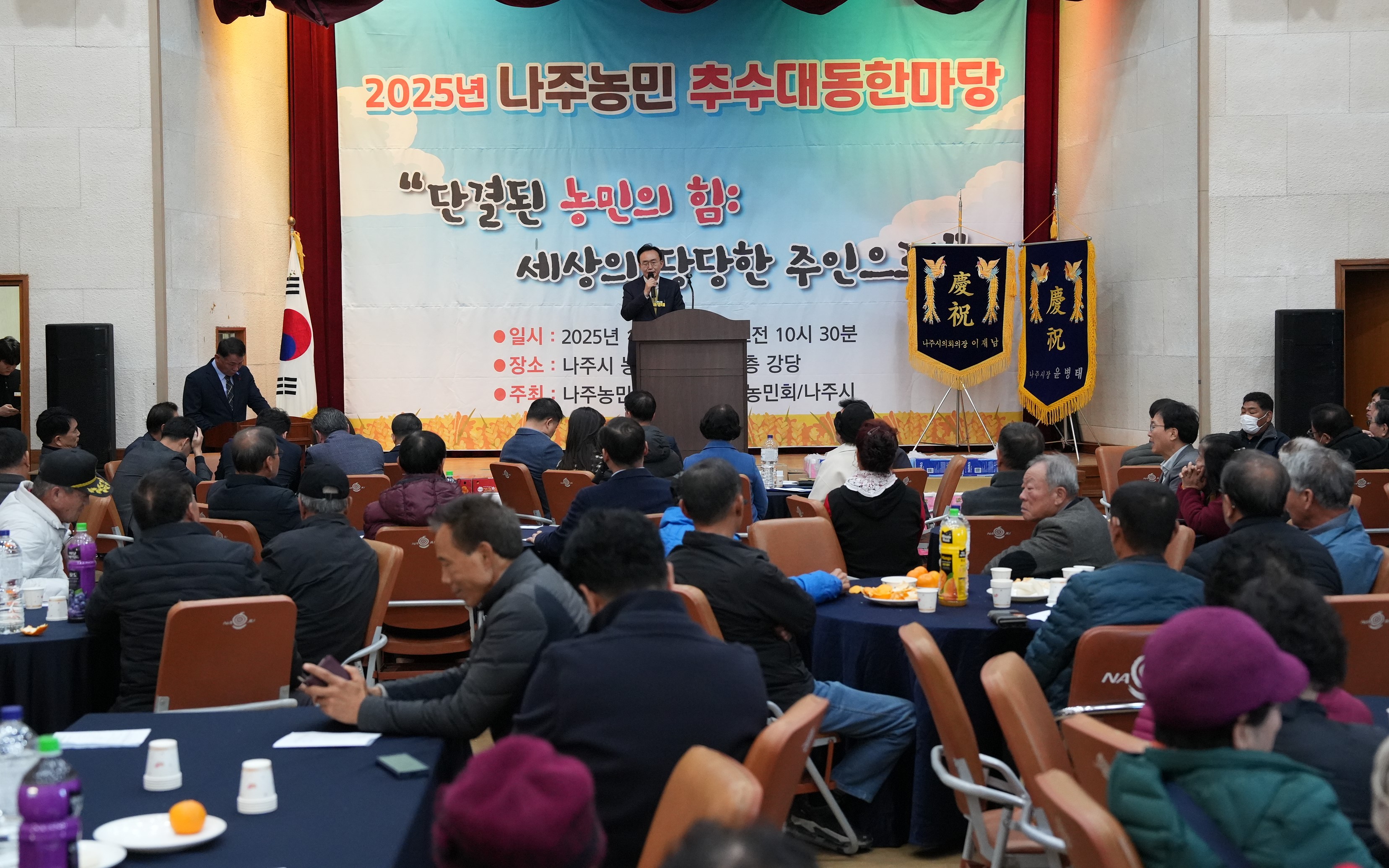 '2025년 나주농민 추수대동한마당' 행사장 전경. 윤병태 나주시장이 단상에서 연설하고 있으며, 원형 테이블에 둘러앉은 많은 농민 참석자들이 경청하고 있다.