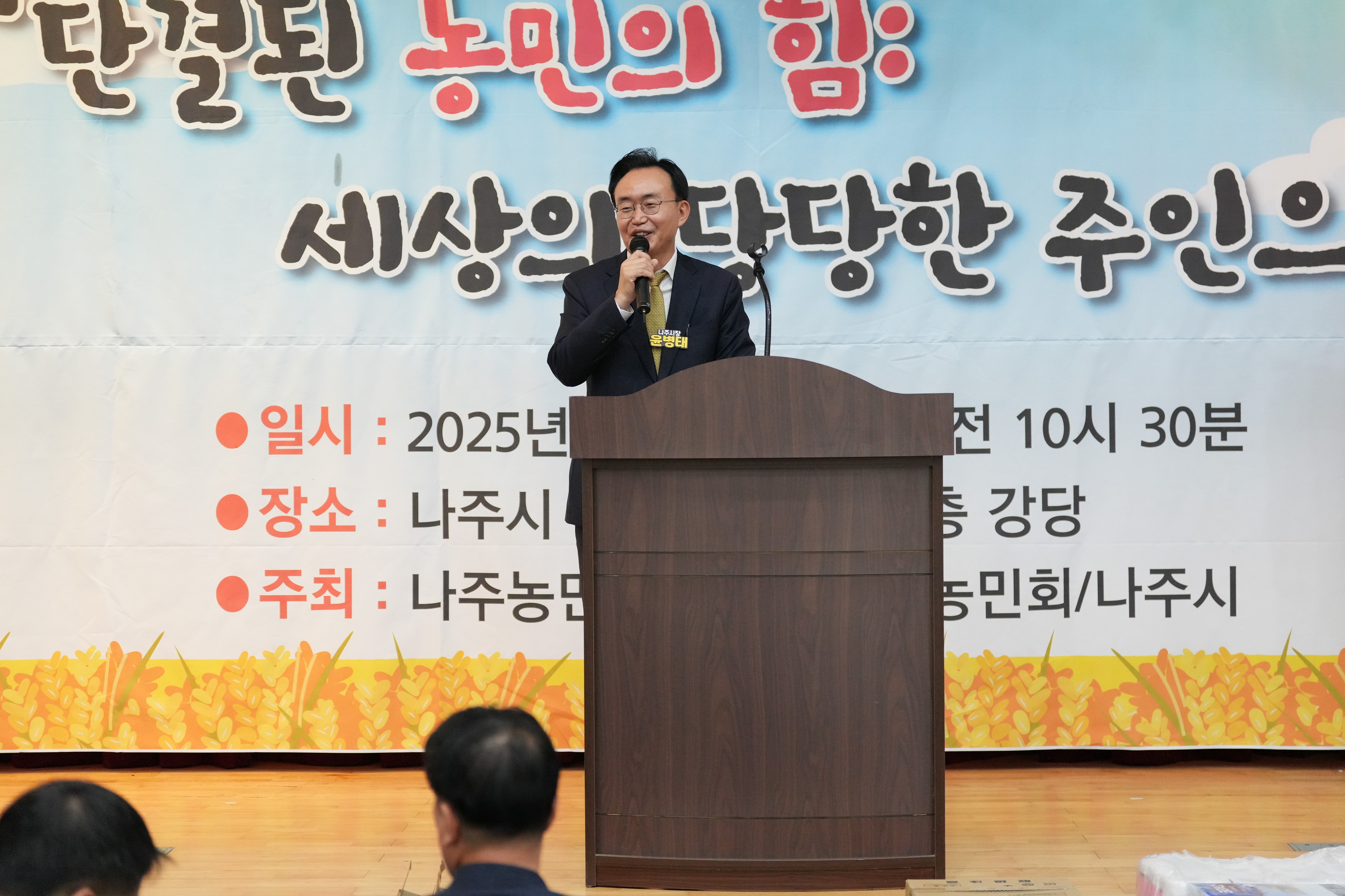 윤병태 나주시장이 단상에 서서 마이크를 잡고 연설하고 있는 모습. 배경에는 '단결된 농민의 힘: 세상의 당당한 주인으로'가 적힌 현수막과 행사 일시가 보인다.