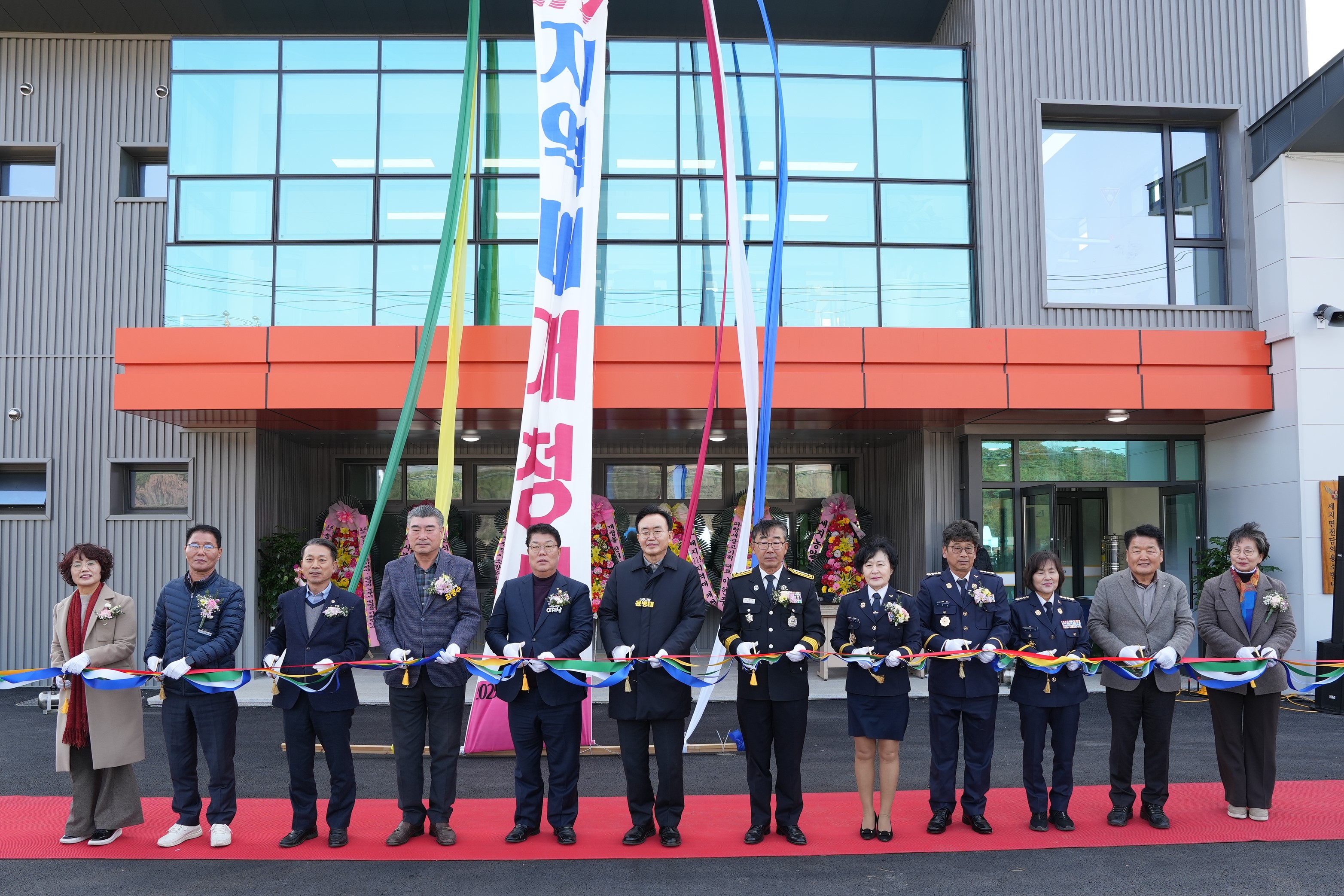 나주소방서 세지 119 지역대 개청식 리본 커팅식 단체 사진. 신축 건물 앞에서 윤병태 나주시장, 소방관, 지역 인사 등 12명이 커팅용 가위를 들고 알록달록한 리본을 자를 준비를 하고 있다. 건물 정면에는 '세지 119 지역대 개청식' 현수막이 길게 걸려 있다.