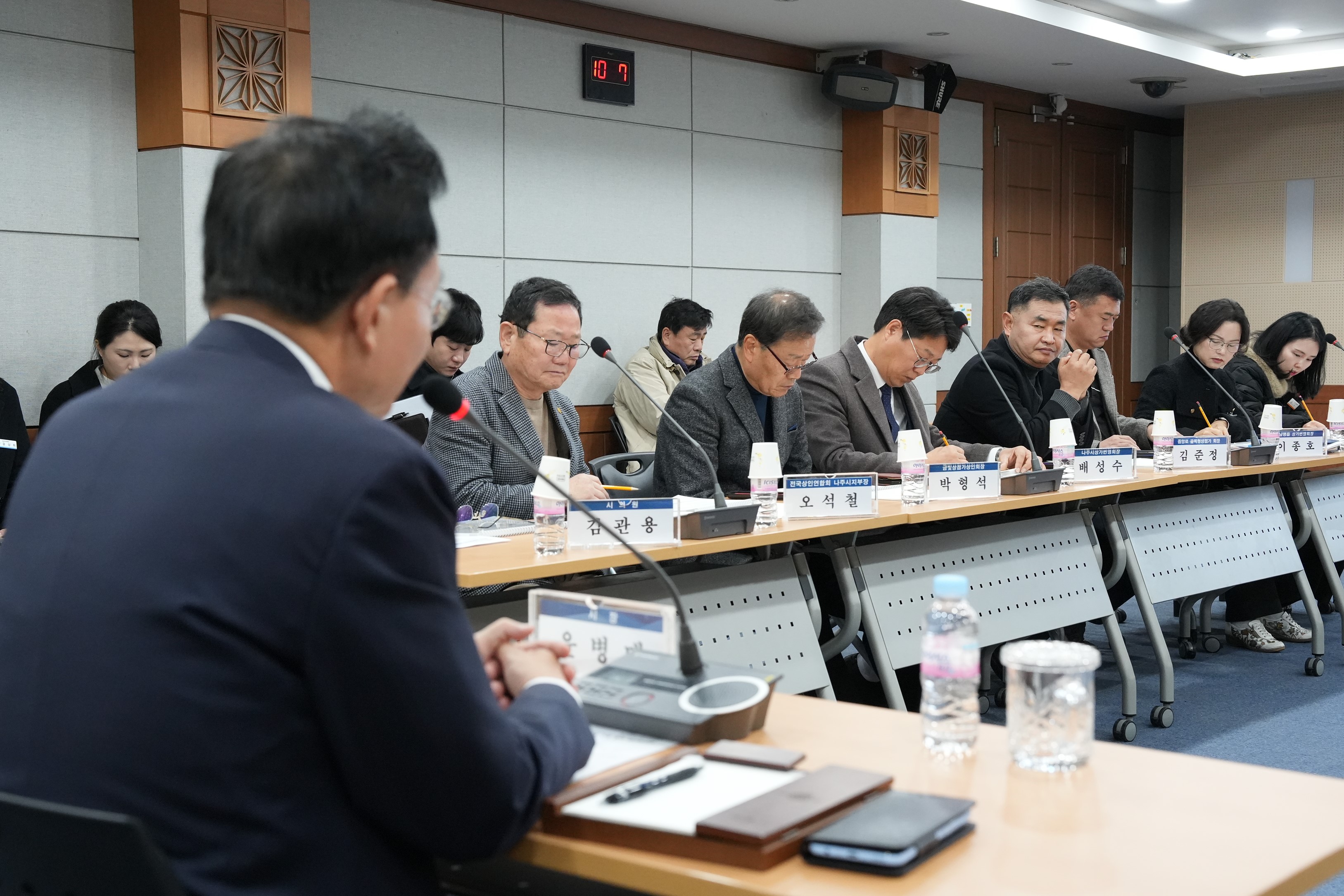  회의 또는 간담회 장면. 테이블에는 참석자들이 앉아 자료를 검토하거나 경청하고 있다.