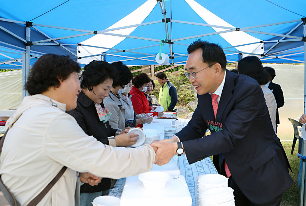 제6회 성북동민의 날 행사 행사장 부스에서 음식 준비를 하고 있는 여성 분과 손을 잡고 인사를 나누는 나주시장 모습