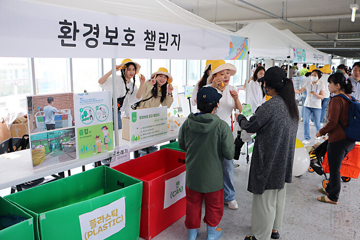 2023년 나주 어린이 큰잔치  행사장에 마련된 환경보호 챌린지 부스의 모습 부스 운영자들과 부스 앞에서 환경 보호 설명을 듣고 있는 아이와 엄마의 모습