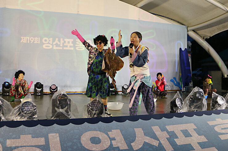 제19회 영산포 홍어축제 개막행사 무대 위에서 진행자와 공연팀이 생물 홍어를 들고 홍어 경매를 잰행하고 있는 모습