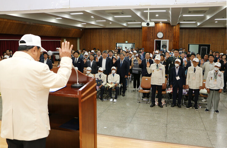 제73주년 6.25전쟁 상기행사 참전자회 임원 분이 결의문 낭독을 하고 있는 뒷모습과 참석자 분들이 서서 오른손을 올려서 함께 결의를 다짐 하고 있는 모습
