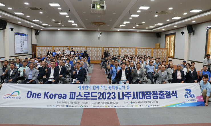 One Korea 피스로드 2023 전남 나주시 통일대장정 출정식  플랭카드를 앞에 두고 참여자들이 앉아서 기념촬영을 하고 있는 모습