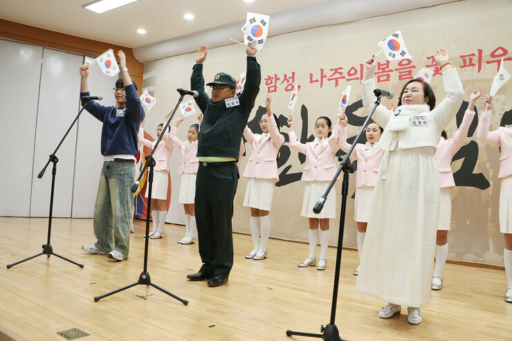 제105주년 3.1절 기념행사 단상 위에서 대표자 남성 2명, 여성 1명과 시립소년소녀합창단이 태극기를 한손에 들고 만세삼창을 하고 있는 모습