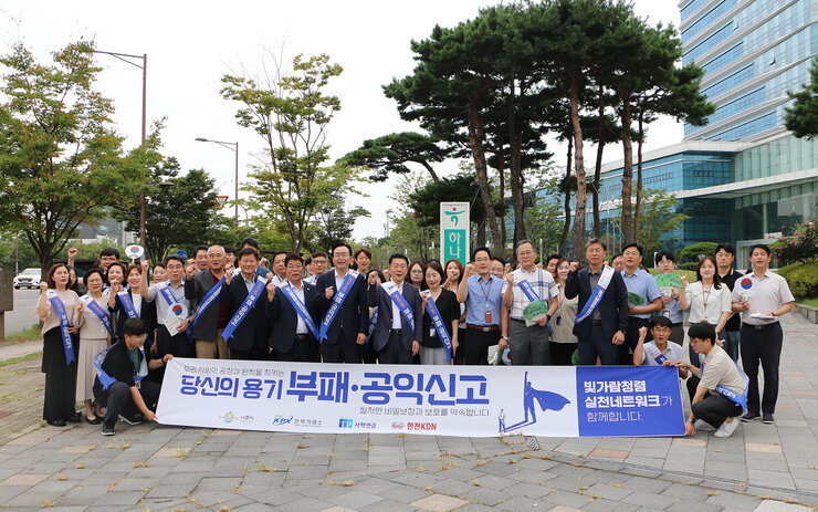 추석맞이 지역상품 판매 촉진 캠페인 및 청렴실천, 고향사랑 기부제 홍보 캠페인 나주시장과 사학연금 사장, 한전 KDN 사장 및 관계자 전체 부패, 공익신고 플랭카드를 펼치고 화이팅을 하며 기념촬영을 하고 있는 모습