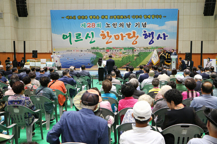 제28회 노인의 날 어르신 한마당 개막식 행사장에 농인회장이 서서 시청 남, 여 직원에게 선서를 받고 있는 모습과 참석자들이 앉아 있는 모습 정면