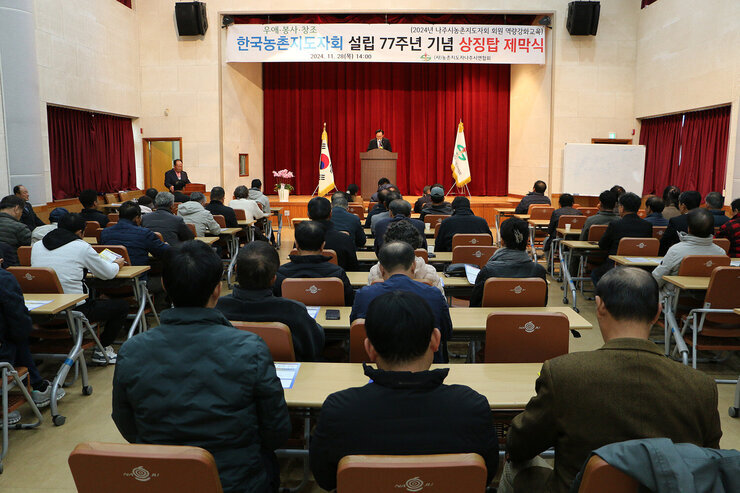 농촌지도자 나주시연합회 상징탑 제막식 나주시장의 축사모습과 참석자들의 앉아 있는 앞모습 정면에서 촬영함