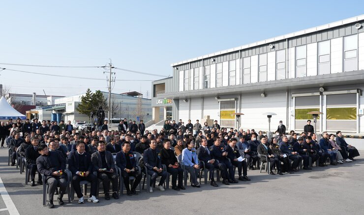 푸드테크 연구지원센터 건립공사 기공식 참석자 전경. 야외 공터에서 많은 참석자들이 일렬로 놓인 의자에 앉아 앞쪽 무대를 향해 경청하고 있다. 뒤쪽으로는 공장 또는 창고 건물들이 보인다.