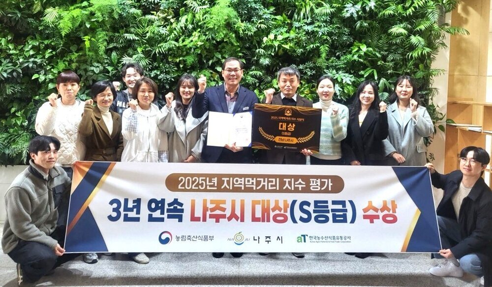 푸른 식물 벽을 배경으로 여러 명의 남녀가 큰 상장과 배너를 들고 서 있는 단체 사진. 가운데 두 남성이 상장을 들고 있고, 그 아래에는 '2025년 지역먹거리 지수 평가', '3년 연속 나주시 대상(S등급) 수상'이 적힌 배너가 있다. 배너 하단에는 '농림축산식품부', '나주시', '한국농수산식품유통공사' 로고와 글자가 보인다.
