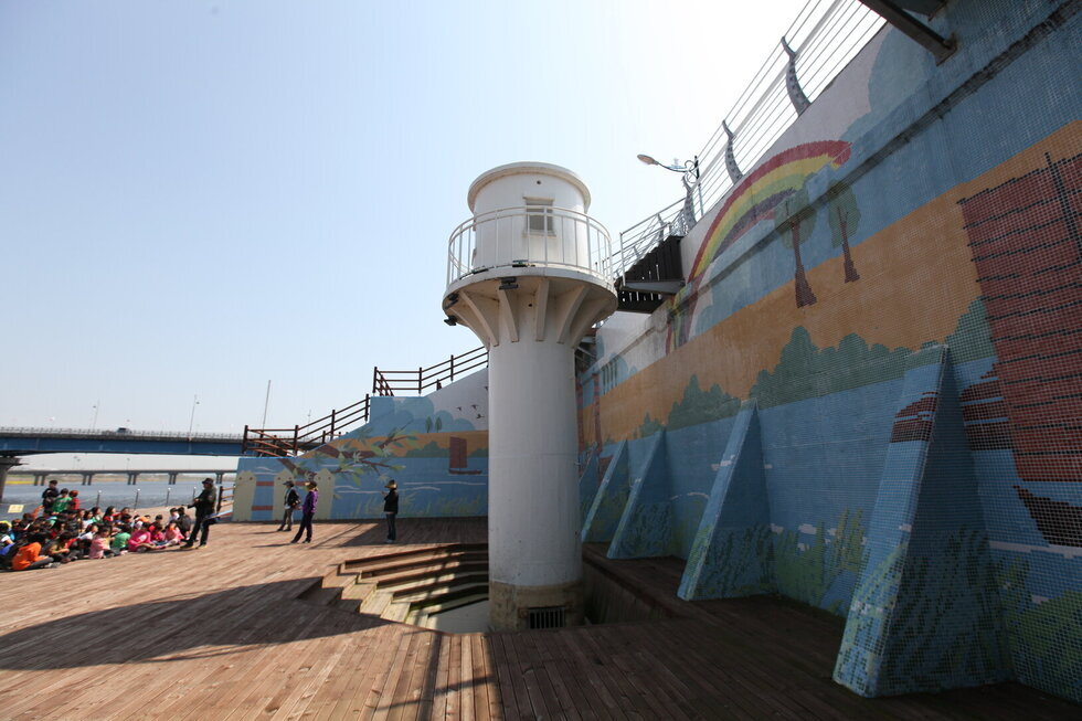 영산포 등대를 찍은 사진. 하얀 등대 옆으로 높은 벽이 있으며 그 앞으로 여러사람들이 앉아 있음.