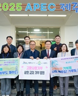 건물 상단에 2025 APEC 제주 라고 적혀 있고 고향사랑 기부제 나도 제주도! 기부도 제주도! 라고 적힌 현수막을 들고 기념촬영하고 있다.