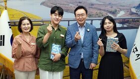 분홍색 블라우스를 입은 중년 여성, 카키색 셔츠를 입고 선물 상자를 든 남성, 윤병태 시장, 검은색 원피스를 입고 선물 상자를 들고 있는 여성이 차례로 서서 손하트를 하고 있다