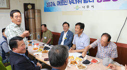 무더위 쉼터 현장 점검 마을 이장 남성 어르신이 자리에 서서 인사말을 하고 있고 미소를 지으며 듣고 있는 나주시장의 모습과 어르신들 