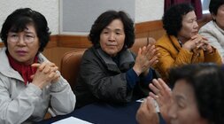  행사에 참석한 중년 여성들 여러 명이 테이블에 앉아 박수를 치거나 주의 깊게 경청하고 있는 모습