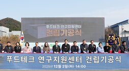  푸드테크 연구지원센터 건립기공식 커팅식 단체 사진. 야외 행사장 무대 아래에서 약 20여 명의 주요 참석자들이 커팅용 흰색 장갑을 끼고 기념 리본을 자르기 위해 서 있다. 배경 스크린에는 '푸드테크 연구지원센터 건립기공식 2025년 12월 2일 (화) 14:00' 문구가 보인다.