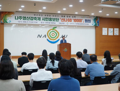 나주영산강축제 시민홍보단 나주시장이 단상에서 인사말을 하고 있는 모습과 참석자들이 앉아서 듣고 있는 뒷모습 전면