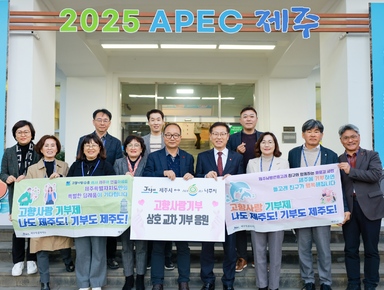 건물 상단에 2025 APEC 제주 라고 적혀 있고 고향사랑 기부제 나도 제주도! 기부도 제주도! 라고 적힌 현수막을 들고 기념촬영하고 있다.