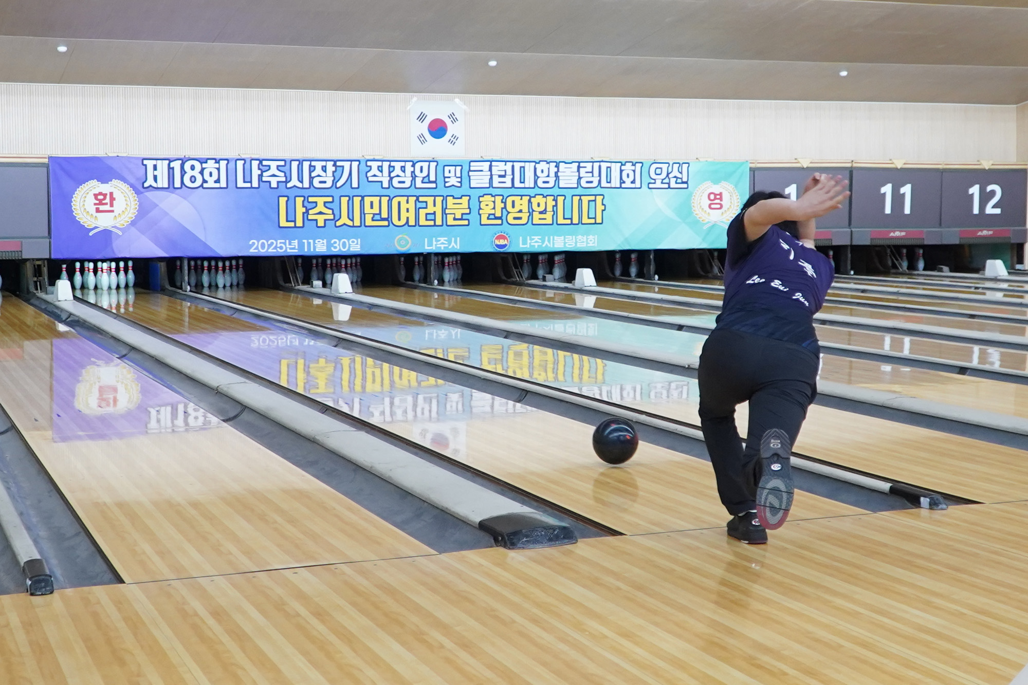 한 선수가 볼링공을 던지는 순간을 포착한 사진. 볼링 레인 위에는 '제18회 나주시장기 직장인 및 클럽대항볼링대회 오신 나주시민여러분 환영합니다' 현수막이 걸려있다.