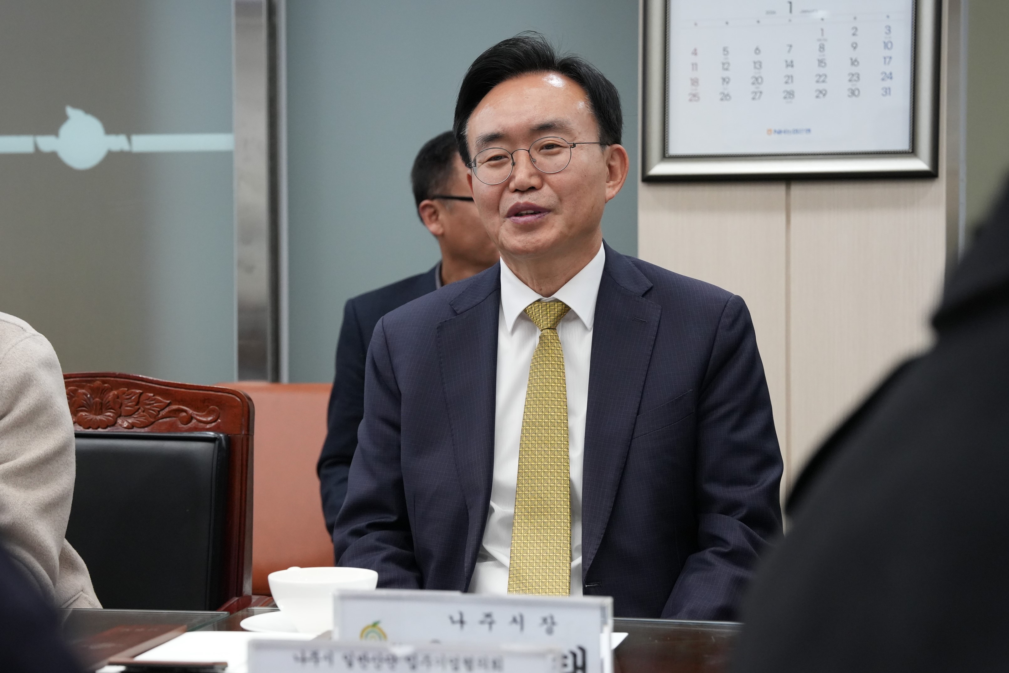  나주시장 명패가 놓인 테이블에 앉아 미소를 짓고 있는 윤병태 나주시장의 클로즈업 사진.