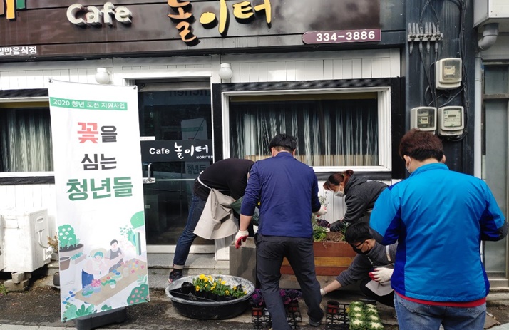 334-3886 cafe놀이터라 적힌 간판 아래 ‘2021년 청년 도전 지원 사업’ 참여자들이 꽃을 심고 있는 모습 옆에 배너(2020 청년 도전 지원사업 꽃을 심는 청년들)가 있는 모습