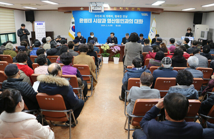 영산동 주민과의 대화 앞쪽의 여성 주민이 건의사항을 말하고 있는 뒷보습과 대화석에 앉아 서 듣으며 필기를 하고 있는 나주시장의 모습과 양 옆의 간부공무원, 면장, 도의원, 시의원이 앉아 있다