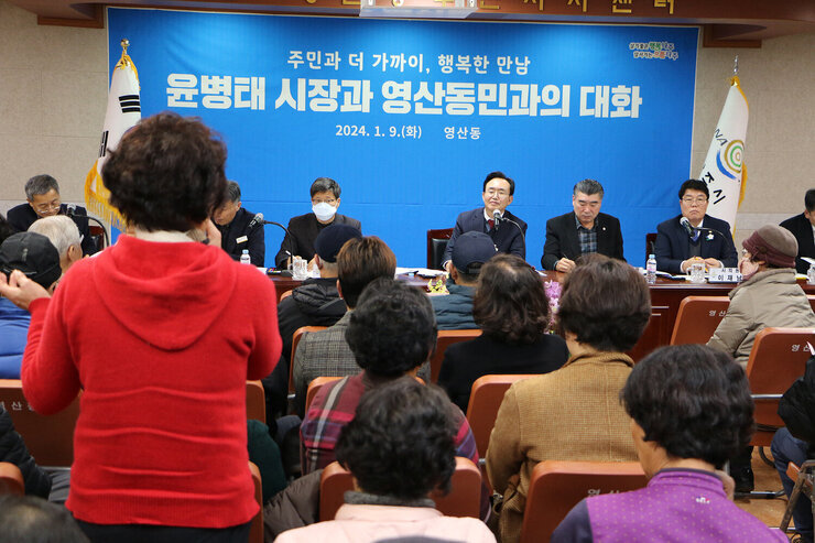 영산동 주민과의 대화 빨간색 상의를 입은 여성 주민이 서서 건의사항을 말하고 있고 나주시장이 듣고 있는 모습과 다른 주민들이 앉아 있는 뒷모습