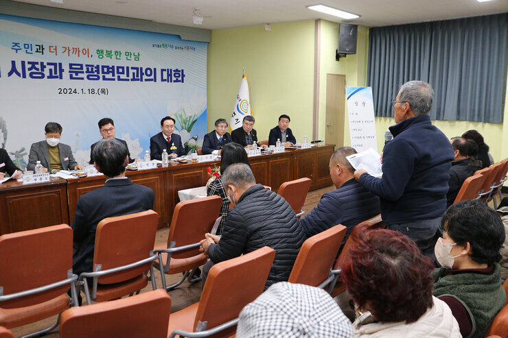 문평면 주민과의 대화 좌측면에서 촬영한 남성 주민의 질의 모습과 대화석에서 바라보고 듣고 있는 나주시장의 모습 양 옆으로 면장, 간부공무원, 시의장, 도의원, 시의원이 보인다