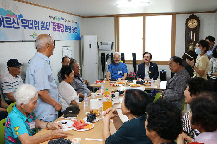 무더위 쉼터 현장 점검 남성 어르신이 자리에 서서 건의사항을 말하고 있는 측면 모습과 듣고 있는 나주시장의 모습 마을 어르신들의 앉아 있는 모습도 함께 보인다