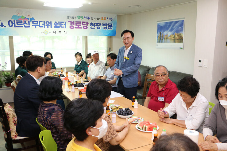 무더위 쉼터 현장 점검 나주시장이 입식테이블 자리에 서서 인사말을 하고 있고 경로당 어르신들이 듣고 있는 모습