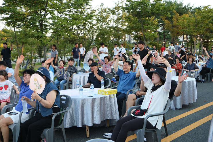 나주 빛가람 하이볼 페스티벌 행사장에 마련된 원형테이블에 앉아 있는 시민들이 EDM 진행자의 호응 유도에 따라 두팔을 머리 위로 올리고 흔들고 있는 모습