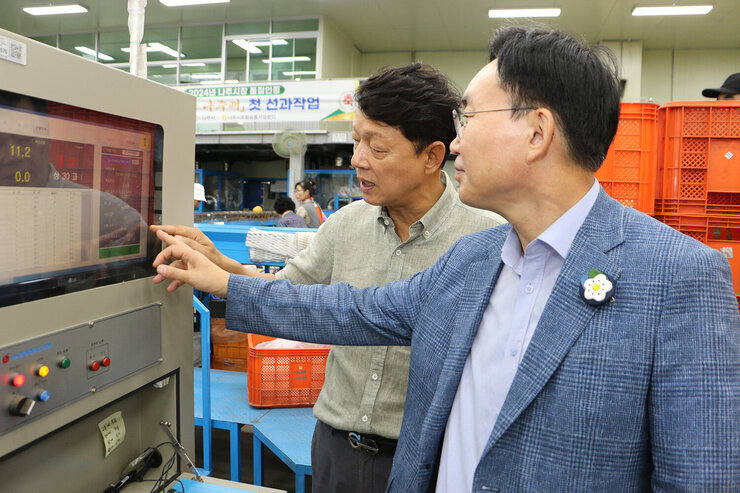 추석 명절 배 선과장 방문 나주시장과 관계자가 컨베이어 기계 앞에서 화면의 측정된 값을 한손으로 가리키며 대화를 나누는 모습