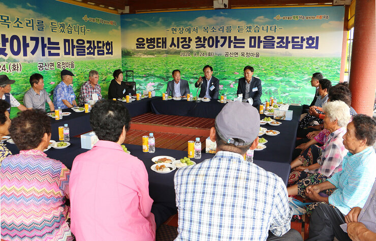 찾아가는 마을좌담회 나주시장이 여성 어르신을 손으로 가리키며 답변을 하고 있는 모습 우산각에 둘러 앉은 어르신들의 모습