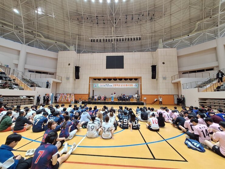 나주시배구협회장배 고등학교 남녀 배구대회 나주시장의 축사모습과 참석 선수들이 배구 코트 바닥에 앉아서 듣고 있는 뒷모습
