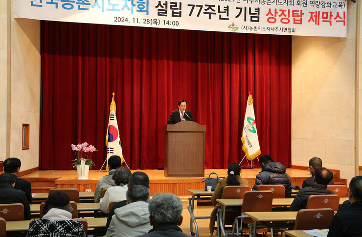 농촌지도자 나주시연합회 상징탑 제막식 나주시장의 축사모습과 참석자들의 앉아 있는 뒷모습 좌측면에서 촬영함