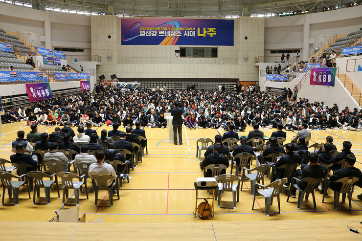제17회 나주 페어컵 배드민턴 대축제 개회식 축사를 하고 있는 나주시장의 뒷편에서 촬영한 모습 참석 동호인들이 앉아 있는 모습 전면