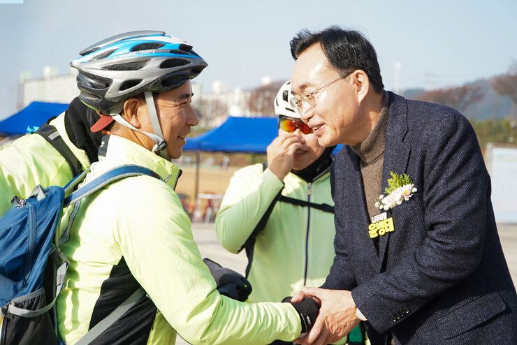  윤병태 나주시장이 자전거와 헬멧을 착용한 젊은 여성 선수들과 야외에서 악수를 나누고 대화하는 모습