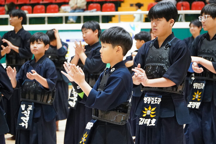  검도 대회에 참가한 소년들이 도복과 호구를 착용한 채 박수를 치고 있다.