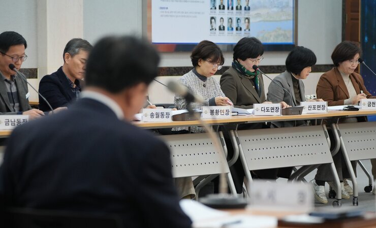 회의에 참석한 사람들이 테이블에 앉아 서류를 보거나 경청하고 있다. 테이블 앞에는 '송월동장', '봉황면장', '다도면장', '신포면장', '금천동장' 등 명패가 놓여 있다.